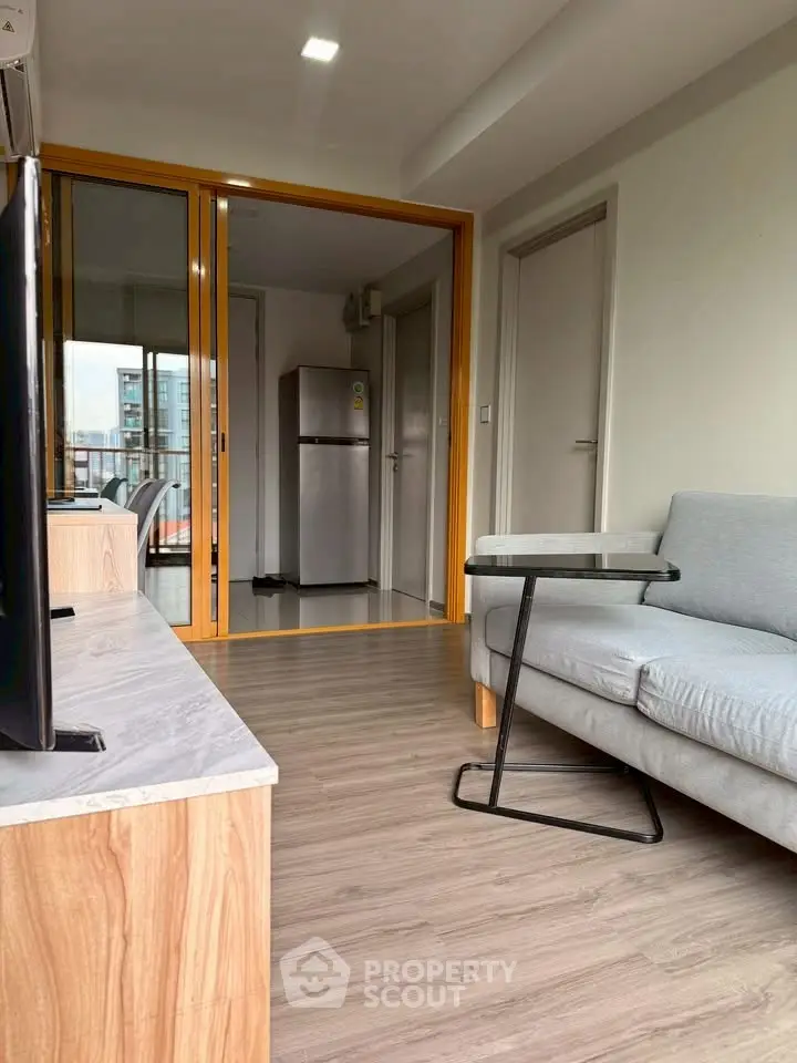 Modern living room with sleek wooden flooring and stylish furniture, featuring a cozy sofa and a compact fridge.