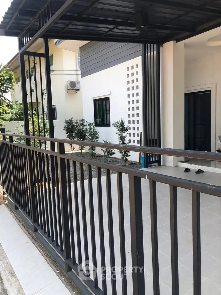 Modern house exterior with sleek metal fence and tiled patio, showcasing contemporary architectural design.