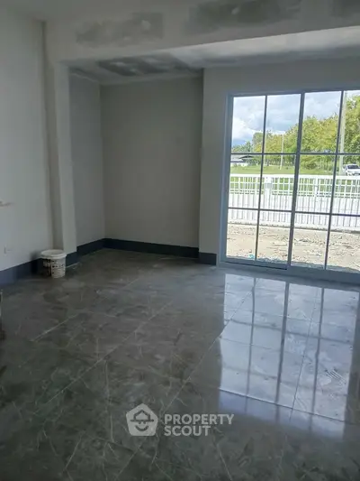 Spacious unfurnished room with large window and glossy tiled floor, offering natural light and outdoor view.