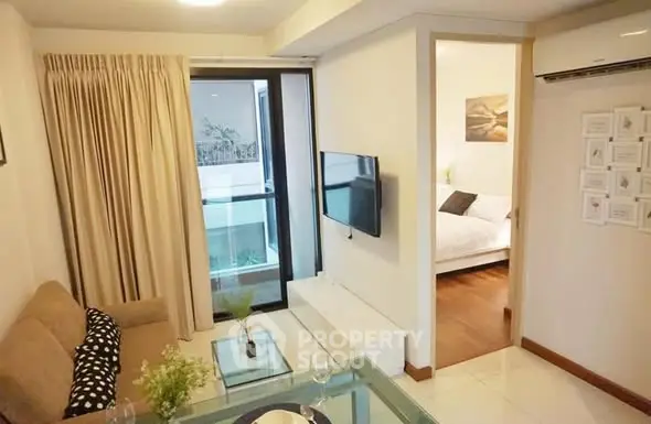 Modern living room with cozy sofa and wall-mounted TV, leading to a bright bedroom.