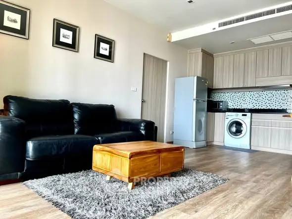 Modern living room with open kitchen, featuring black leather sofa and wooden coffee table.