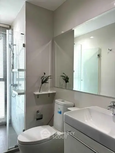 Modern bathroom with sleek fixtures and large mirror, featuring a glass shower enclosure.