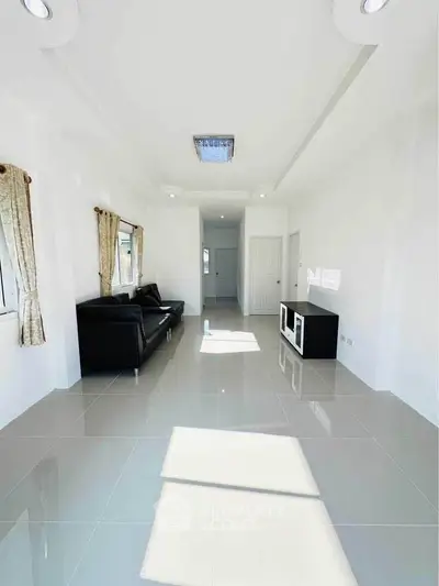 Spacious and bright living room with modern black sofa and sleek tile flooring.