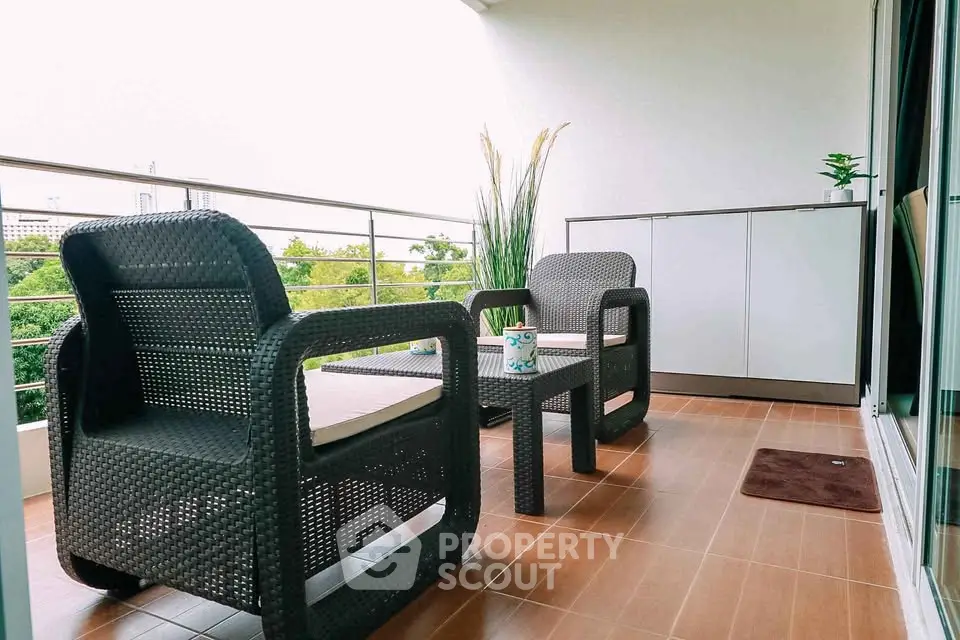 Spacious balcony with stylish outdoor seating and lush greenery view.