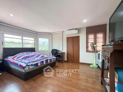 Spacious bedroom with wooden flooring and large windows offering natural light.