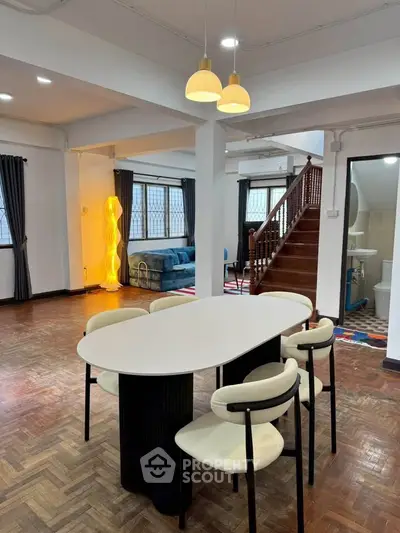 Spacious open-plan living area with modern dining set and cozy seating, featuring stylish lighting and wooden flooring.