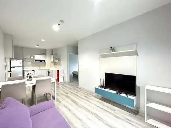 Modern open-plan living room with kitchen, featuring sleek furniture and bright lighting.