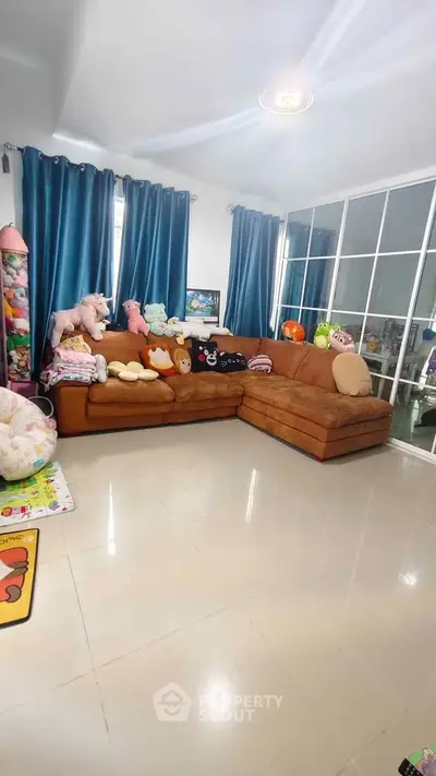 Spacious living room with cozy brown sectional sofa and plush toys, featuring large windows and elegant blue curtains.