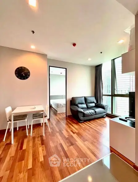 Modern living room with wooden flooring, cozy seating, and dining area in a bright apartment.