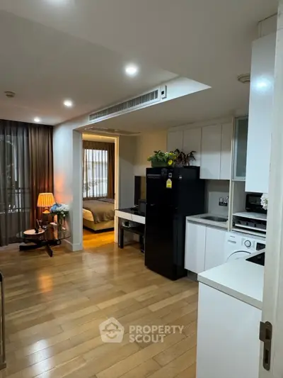 Modern open-plan living room with kitchen and bedroom, featuring wooden floors and sleek appliances.