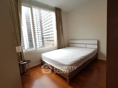 Modern bedroom with large window and city view, featuring wooden flooring and minimalist decor.