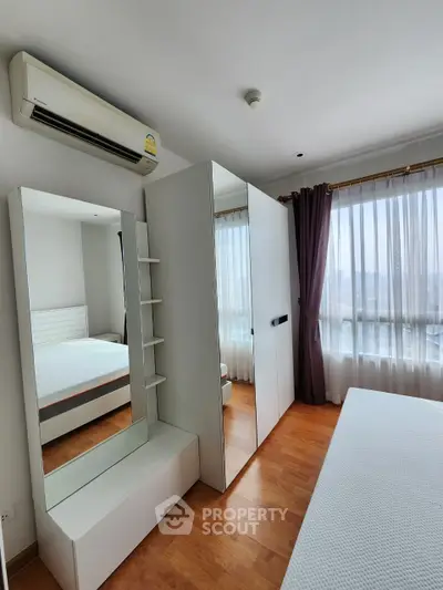 Bright bedroom with large mirror and wardrobe, featuring wooden flooring and air conditioning.