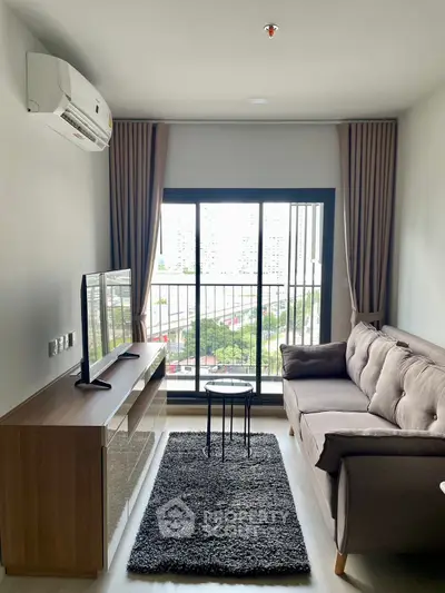 Modern living room with large window, cozy sofa, and sleek TV setup in a high-rise apartment.