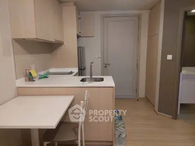 Modern compact kitchen with light wood cabinetry and sleek appliances in a cozy apartment.