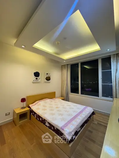 Modern bedroom with cozy lighting and city view from large window.