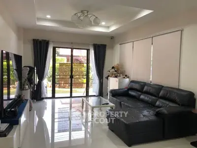 Spacious living room with modern black leather sofa and large windows overlooking garden.