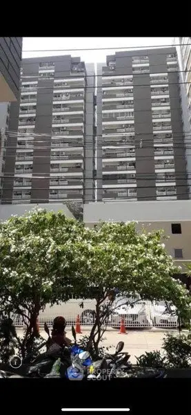 Modern high-rise building exterior with lush greenery and parked vehicles in urban setting.