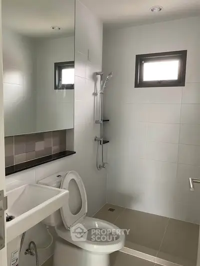 Modern bathroom with sleek fixtures and minimalist design, featuring a shower and compact layout.