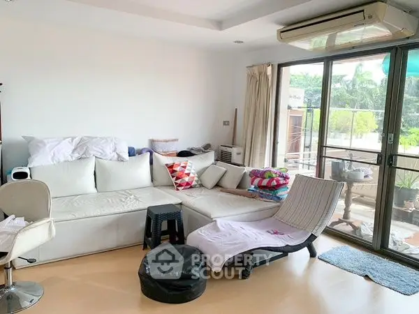 Spacious living room with modern furniture and large windows opening to a balcony with garden view.