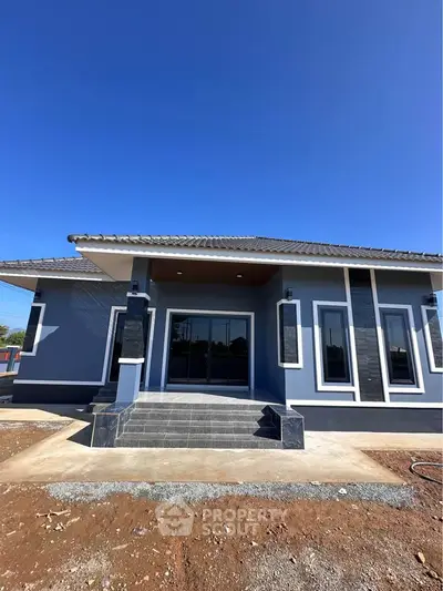 Modern single-story house with sleek design and spacious entrance under clear blue sky.