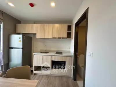 Modern compact kitchen with wooden cabinets and integrated appliances in a cozy apartment setting.