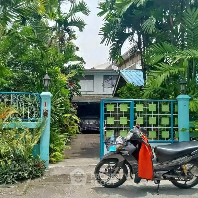 Charming tropical home entrance with lush greenery and secure gate.