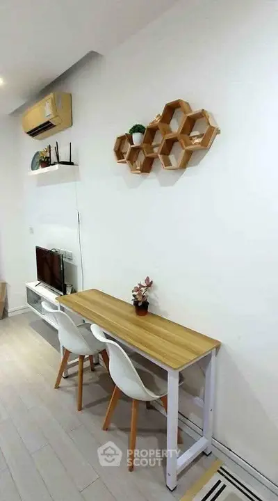 Modern minimalist living room with stylish furniture and wall decor, featuring a compact dining area and air conditioning.