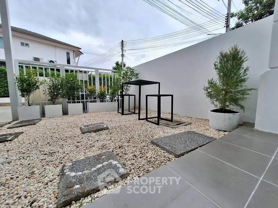 Modern minimalist garden with pebble landscaping and sleek metal furniture in a serene residential setting.