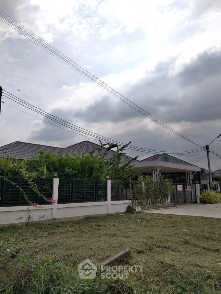Modern suburban house with lush greenery and spacious driveway under cloudy sky.