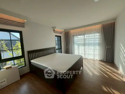 Spacious bedroom with large windows and elegant curtains, featuring a modern bed and wooden flooring.