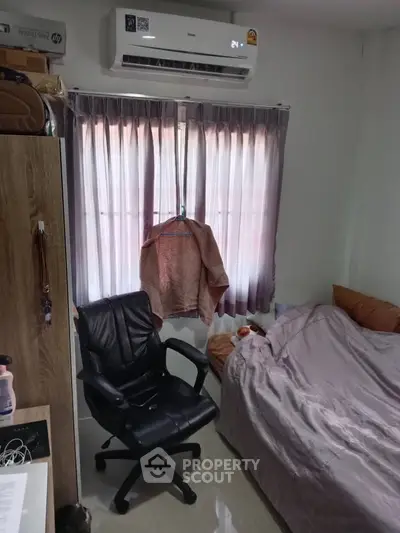 Cozy bedroom with air conditioning and natural light through curtains, featuring a comfortable chair and tidy bed.