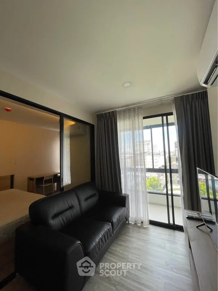 Modern living room with black leather sofa and city view balcony in a stylish apartment.