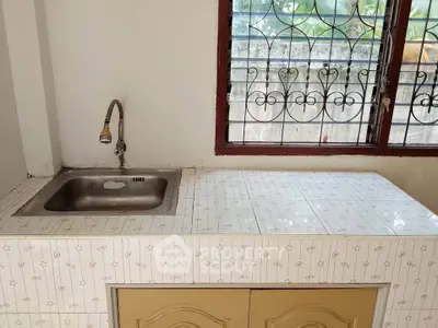 Charming kitchen with tiled countertop and stainless steel sink, featuring a window with decorative grill.