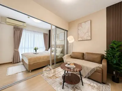 Modern bedroom with cozy sofa and stylish decor, featuring large mirrored wardrobe and natural light.