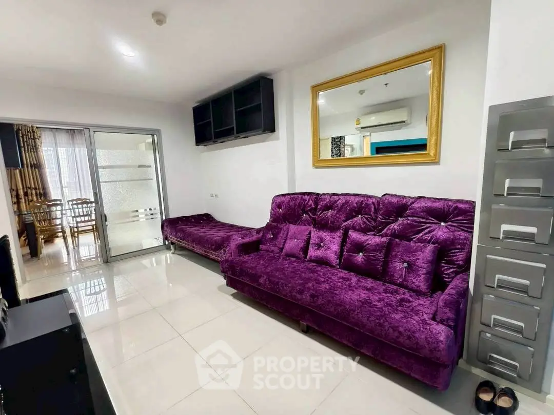 Modern living room with plush purple sofa and sliding glass doors leading to dining area.