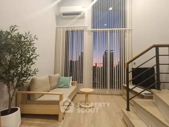 Modern living room with high ceiling, large windows, and stylish decor at sunset.