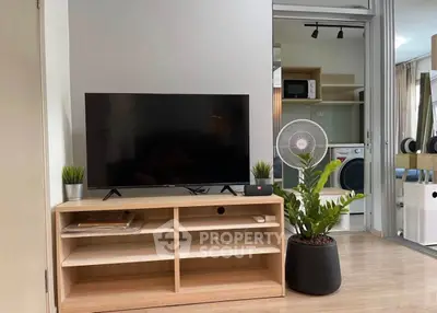 Modern living room with TV, plants, and laundry area in background.