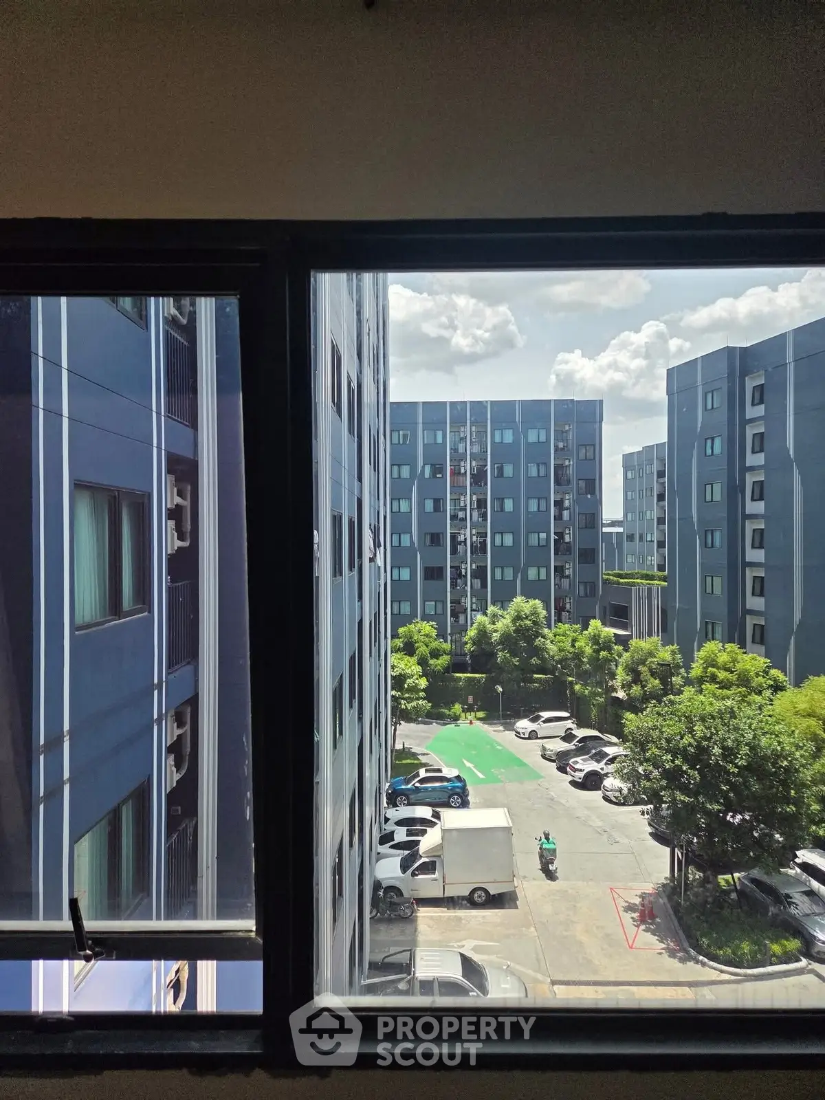 Modern apartment complex view from window with parking area and lush greenery.