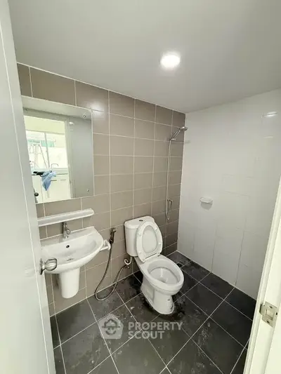 Modern bathroom with sleek fixtures and neutral tiles, featuring a shower and toilet in a compact layout.