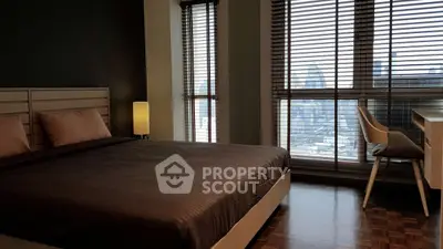 Modern bedroom with city view, featuring sleek furniture and large windows with blinds.