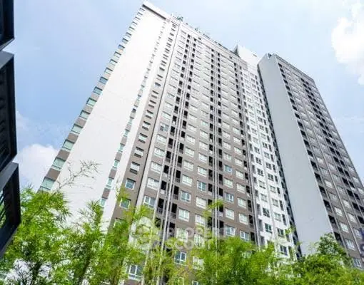 Modern high-rise apartment building with lush greenery and clear blue sky.