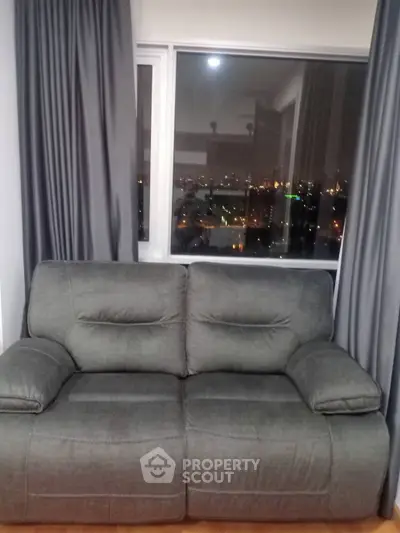 Cozy living room with plush gray sofa and city view through large window, perfect for relaxation.
