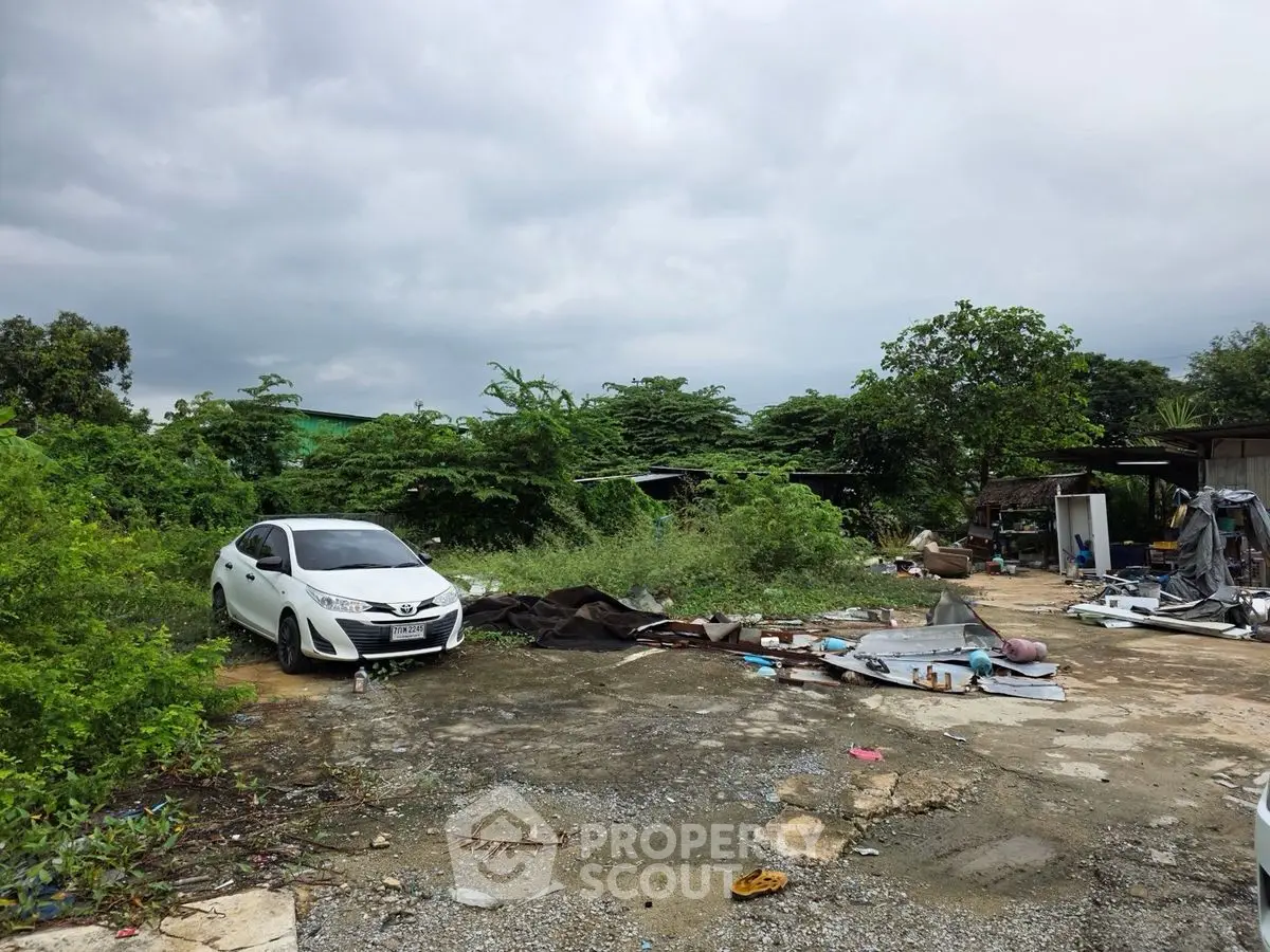 Spacious outdoor area with greenery and potential for development, featuring a parked car and scattered materials.