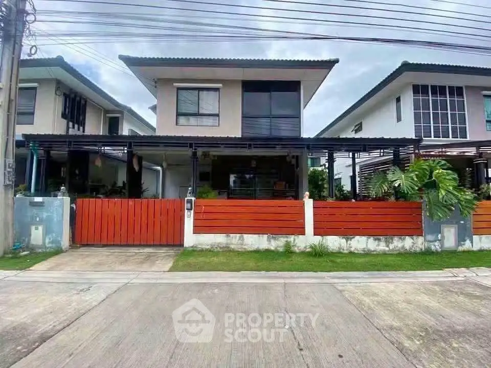 Modern two-story house with red fence and lush greenery in suburban neighborhood.