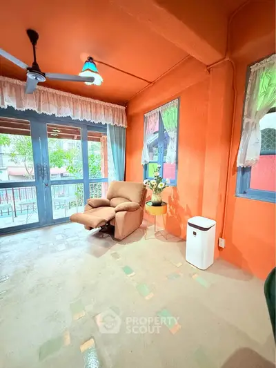Charming living room with vibrant orange walls, cozy armchair, and large windows offering natural light.