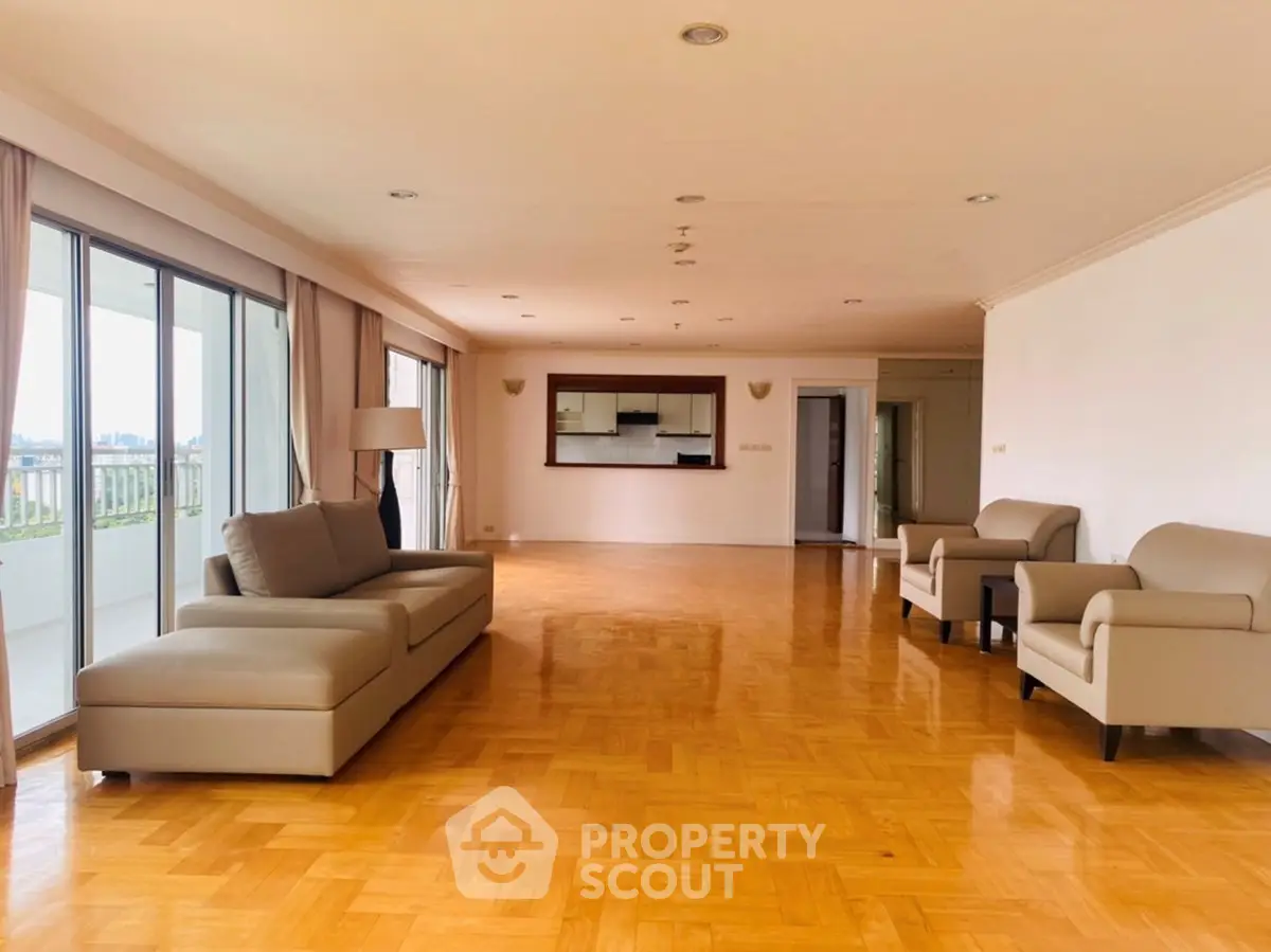 Spacious living room with parquet flooring and large windows leading to a balcony.
