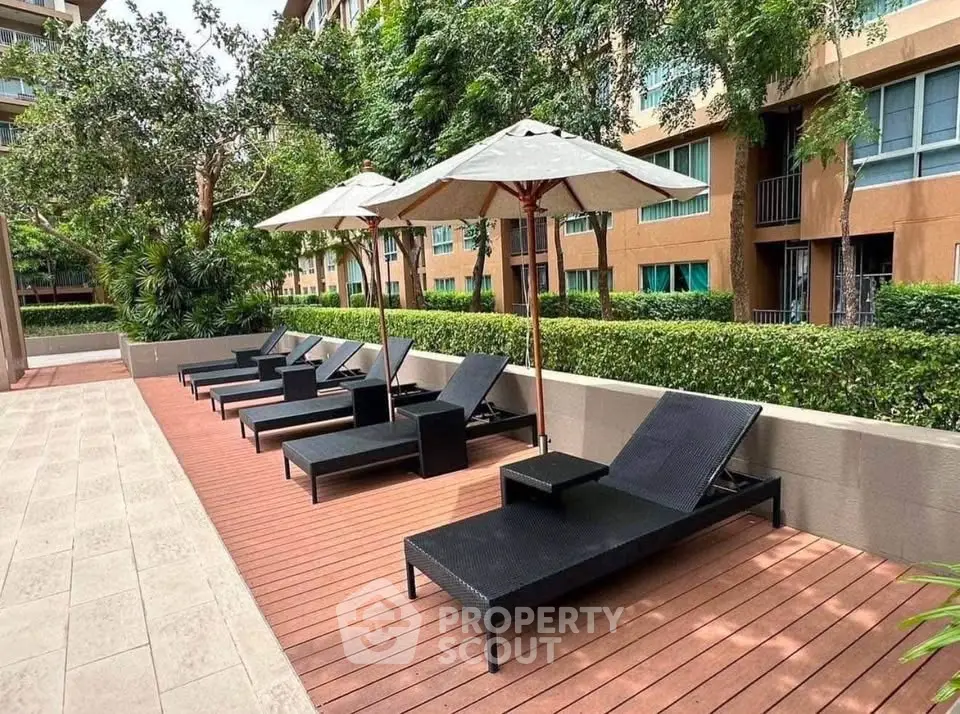 Luxurious outdoor poolside area with stylish lounge chairs and umbrellas in a modern apartment complex.