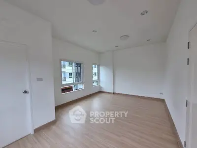 Spacious empty room with wooden flooring and large windows in modern apartment.