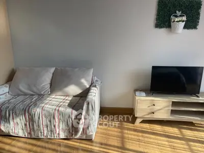 Cozy living room with sofa and TV stand, natural light streaming in.