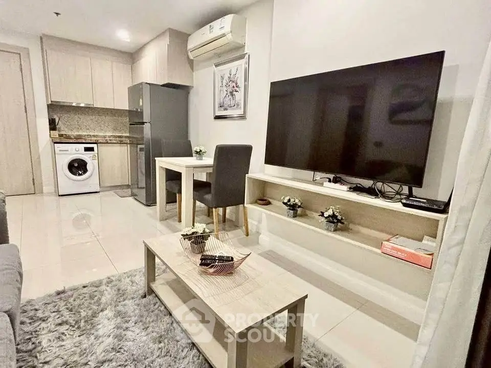 Modern living room with open kitchen, featuring a large TV and washing machine.